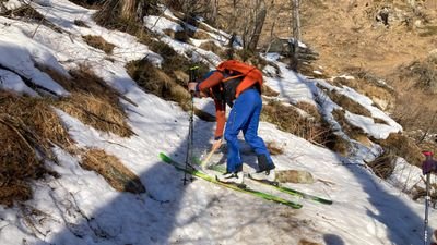 Person with skis and backpack on snow-covered slope in mountainous landscape.