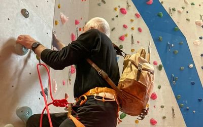 Person climbing in a hall with a climbing harness and rope, colorful holds on the wall.
