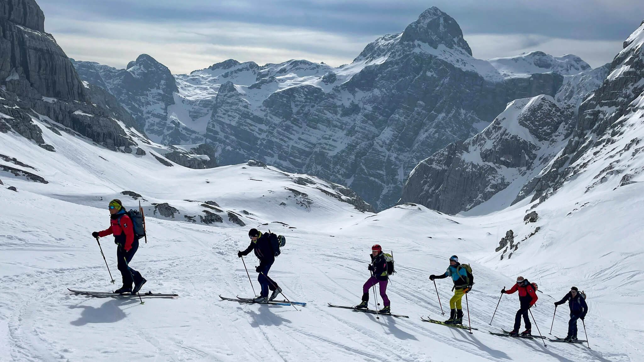 Personen mit Skiern und Rucksäcken steigen in verschneiten Bergen auf.