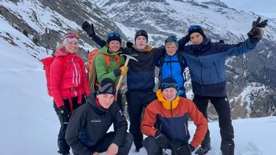 Group of people with winter clothing and backpacks in snow-covered mountains.