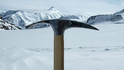 Ice axe in the snow in front of a snowy mountain landscape in Switzerland.