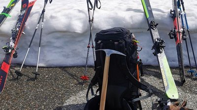 Ski equipment with skis, poles, backpack, and ice pick placed in front of a snow wall.