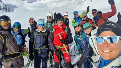 Group of people with ski equipment and helmets posing in the snowy mountain area.