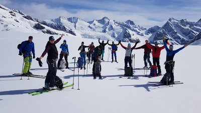 Group of skiers with helmets and poles on a snow-covered mountain with an Alpine backdrop.