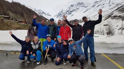 Group of people in winter clothing posing on a street in front of snow-covered mountains.
