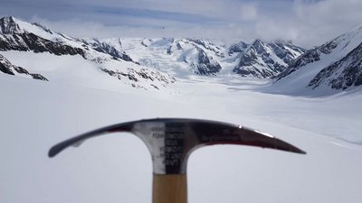 Ice pick in front of a snow-covered mountain landscape with glaciers and cloudy sky in the background.