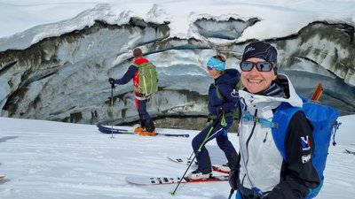 People with skis and helmets are standing in front of a crevasse in snow-covered mountains.