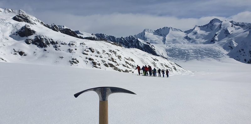 Group of people with mountaineering equipment on a snowy glacier, ice axe in the foreground.
