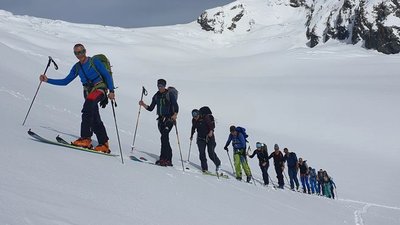 Group of people ski touring in snowy mountains, with ski poles and backpacks.