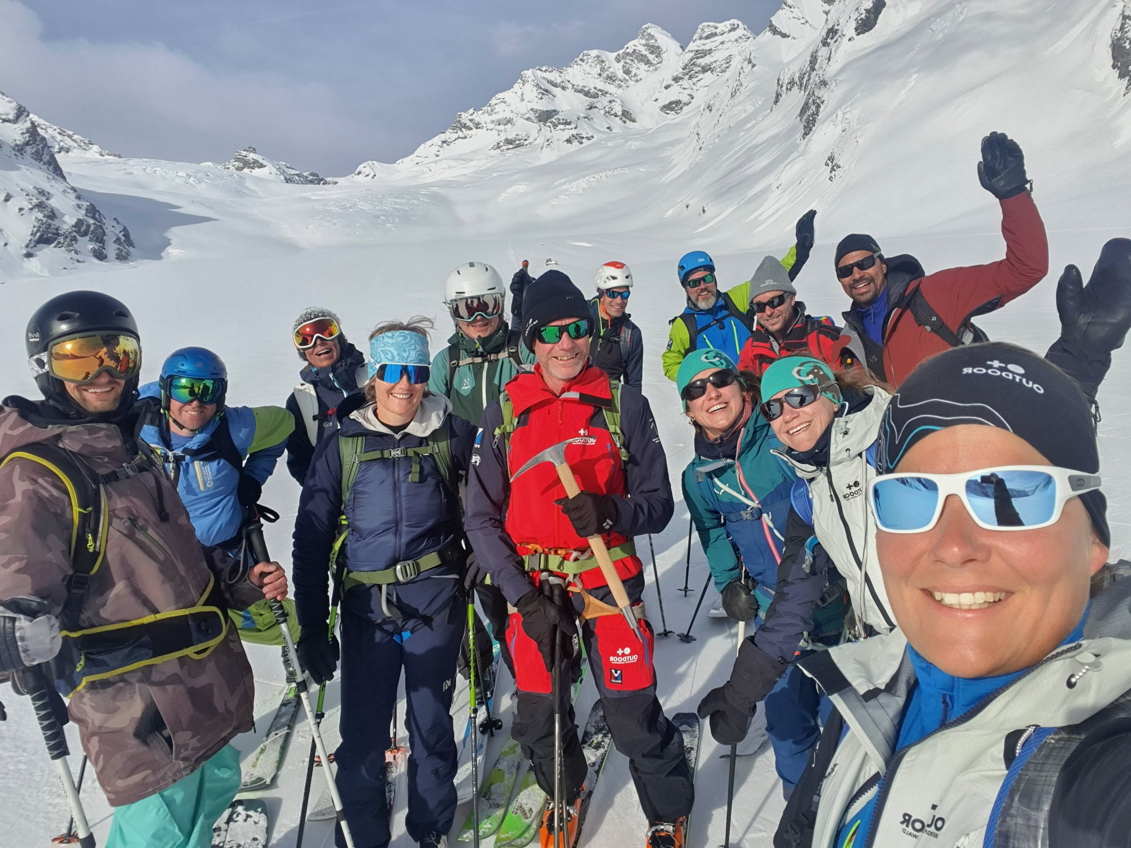 Gruppe von Skifahrern mit Helmen und Skibrillen in verschneiten Bergen.