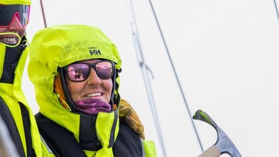 People in yellow jackets and sunglasses on a sailboat, holding a sail tool.
