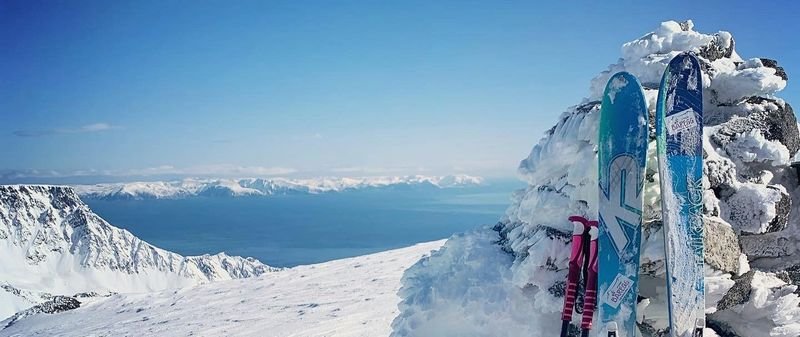 Two skis and poles lean against a snow-covered rock in a mountain landscape.