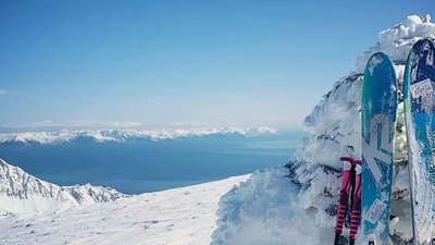Two skis and poles lean against a snow-covered rock in a mountain landscape.