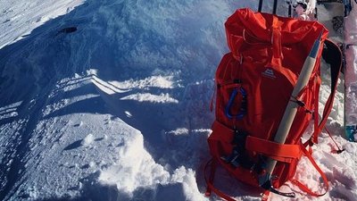 Red backpack with ice pick and skis on snow-covered mountain.