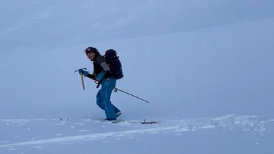 Person with a backpack and ice pick hiking in the snow. Wearing winter clothes and a hat.