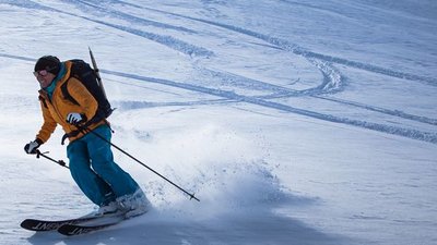 Person on skis with a helmet and backpack is skiing down a snowy mountain slope.