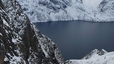 Snow-covered mountain landscape with a view of a lake, surrounded by rugged cliffs.