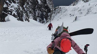 People with skis and helmets are climbing in the snowy mountain terrain.