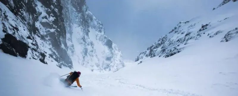 Person skiing in a snow-covered mountain valley, wearing a helmet and ski equipment.
