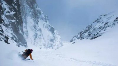 Person skiing in a snow-covered mountain valley, wearing a helmet and ski equipment.