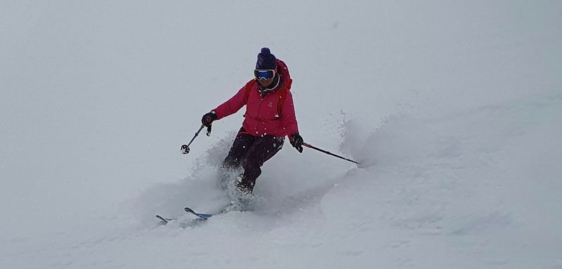 Person on skis with helmet and ski goggles is skiing through a snowy mountain landscape.