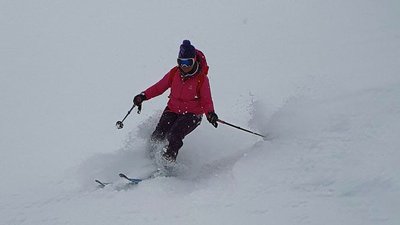 Person on skis with helmet and ski goggles is skiing through a snowy mountain landscape.