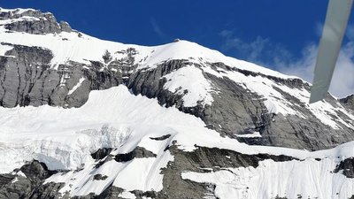 Snow-covered mountain landscape with rock walls and glaciers under a blue sky.