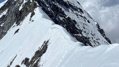 Snow-covered mountain peak in the Alps with steep rock walls and clouds in the background.