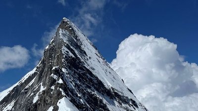 Snow-covered mountain peak under a blue sky with clouds in the background.