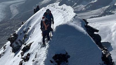 Mountaineers with helmets and ropes on a snow-covered ridge in an alpine mountain landscape.