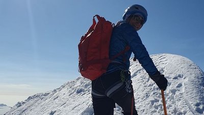 Person with helmet and backpack climbing on a snow-covered mountain peak.