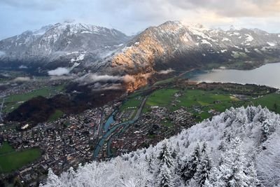 Aerial view of a snowy mountain valley, town, river, and lake in Switzerland.