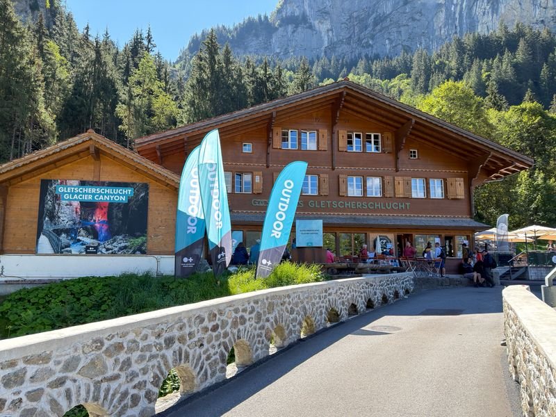 Visitors outside the Glacier Canyon building in Grindelwald, with flags and mountains behind.