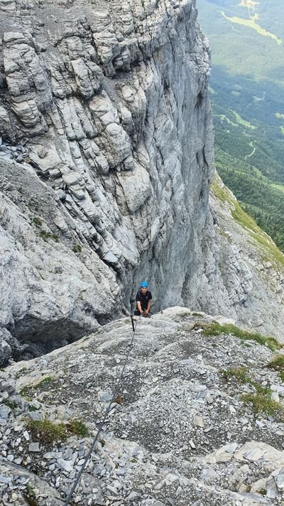 Climber in blue helmet ascending a roped rocky alpine cliff.