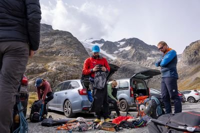 Mehrere Personen mit Kletterausrüstung und Helmen bereiten sich neben Autos in bergiger Landschaft vor.