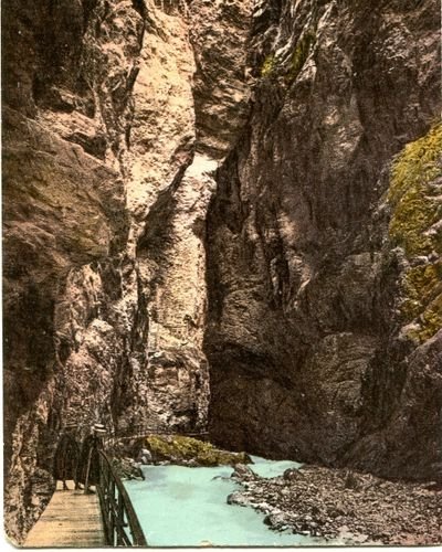 Wooden walkway with railing along steep rocky canyon walls above a turquoise river, with cliff stairs visible.