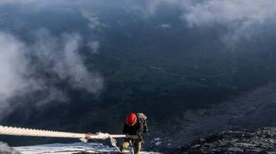 Kletterer mit rotem Helm und Seil an vereister Felswand über dem Tal