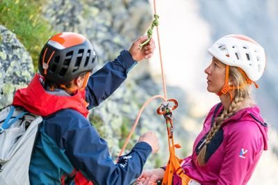 A mountain guide explains abseiling equipment to a guest.