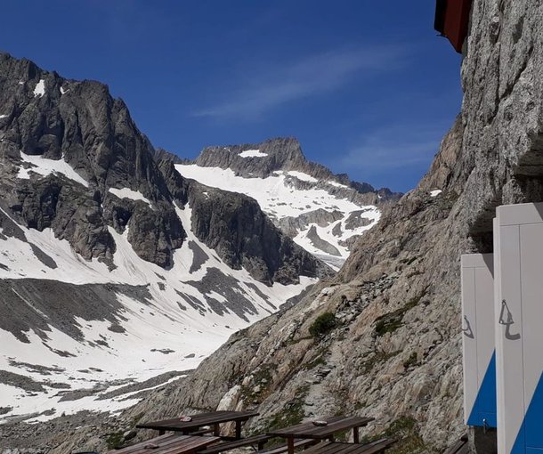 Snow-covered mountains with rocky peaks, adjacent to a stone building and picnic tables.