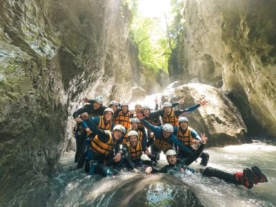 Canyoning group posing with laughter in wetsuits in a narrow rock gorge in the water