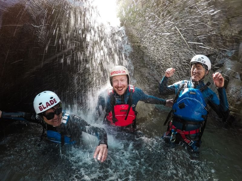 Three people laughing under a waterfall while canyoning in a gorge.