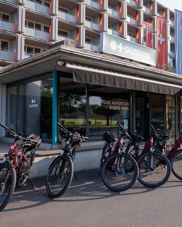 Bicycles parked outside an adventure company building with signage and a multi-story structure behind.