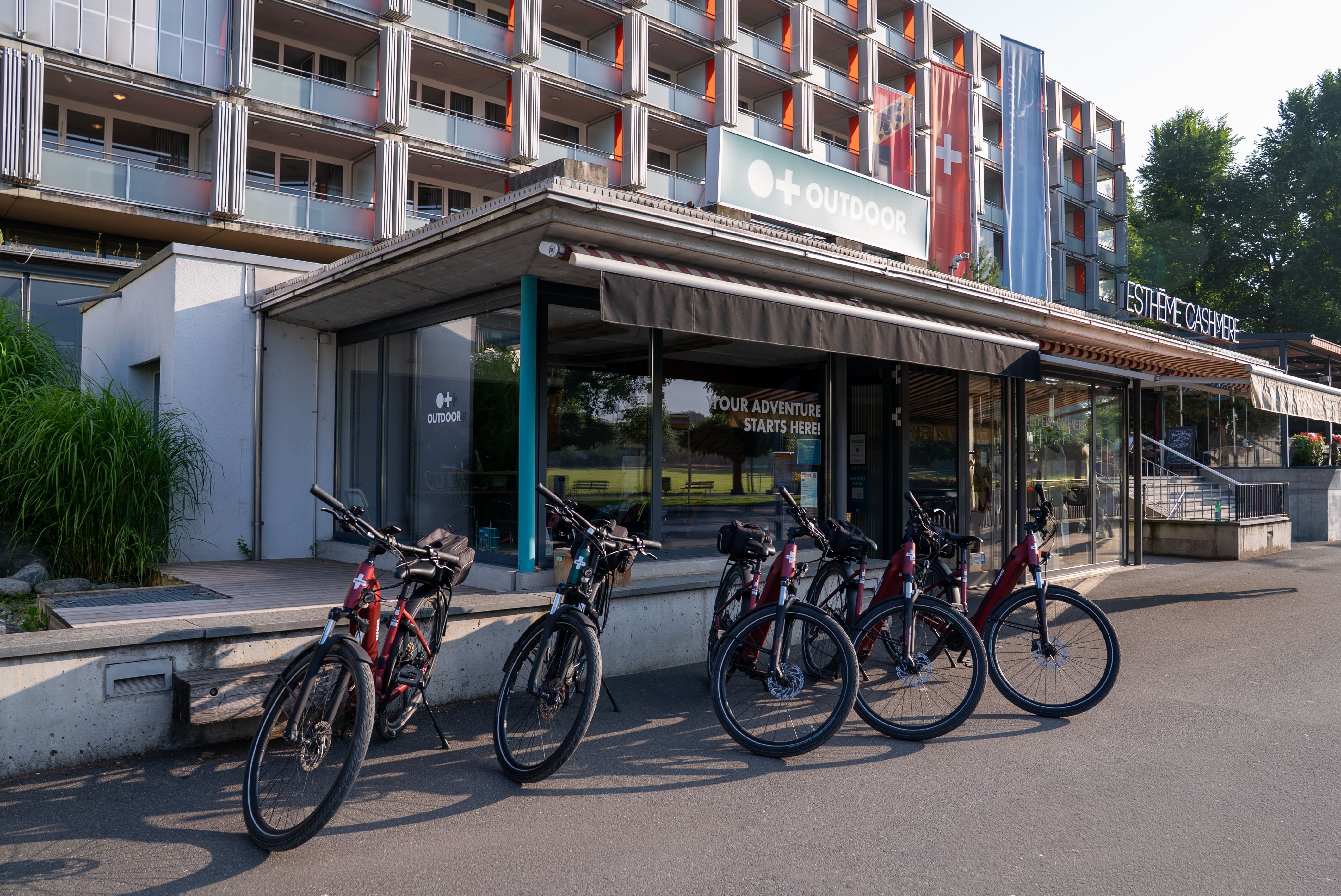 Fahrräder stehen vor einem Gebäude eines Abenteuerunternehmens mit Beschilderung und einem mehrstöckigen Gebäude im Hintergrund.