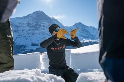 Person in Winterkleidung mit Handschuhen im Schnee, umgeben von Bergen, baut Schneeblöcke.