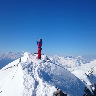 A man is standing on a mountain peak (Wildhorn) and taking a photo. In the background, other peaks of the Alps can be seen.