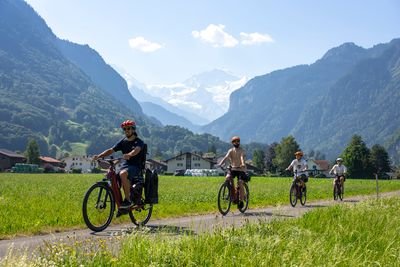 Vier Personen fahren mit Helmen auf E-Bikes auf einem Weg in einem grünen Tal mit Bergen im Hintergrund.