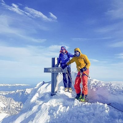 Zwei Personen stehen beim Gipfelkreuz auf einem Berggipfel - dem Finsteraarhorn.