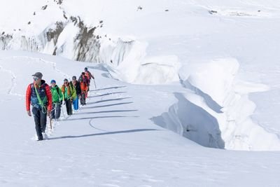 Group with helmets and ropes hikes across snowy glacier landscape in the mountains.