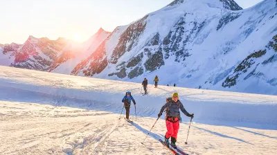 Skitourengänger im Aufstieg mit Sonnenaufgang im Hintergrund