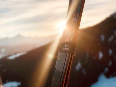 Skiing in front of a mountain landscape at sunset, snow visible on the mountain peaks.